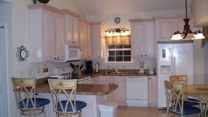 A kitchen with white cabinets, a central island with bar stools, a clock, and a window with a checkered valance. - Fun In the Sun ~ Ocean Lakes  (Myrtle Beach)