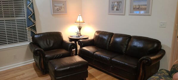 A living room with a brown leather sofa, a matching armchair, and an ottoman. There is a small table with a lamp between them. - Fun In the Sun ~ Ocean Lakes (Myrtle Beach)