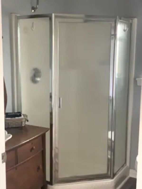 A room with a walk-in closet, a wooden dresser, and a glass shower enclosure. - Charming Cottage in the heart of Wine Country (Temecula)