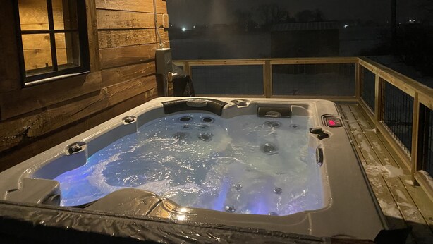 Un bain à remous sur une terrasse en bois, avec un chalet en bois en arrière-plan.