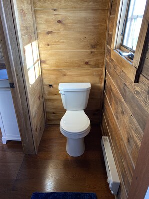 Un baño pequeño con paneles de madera, un inodoro blanco, una ventana y un radiador.