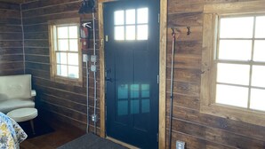 L’intérieur d’une cabane en rondins, avec une porte noire, deux fenêtres, une chaise et une table.