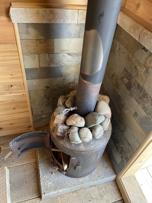 Una estufa de leña con chimenea metálica, rodeada de piedras y virutas de madera.