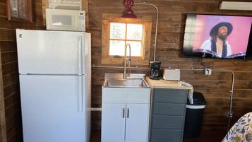 Cocina compacta con refrigerador, microondas, pileta y televisor montado en la pared.