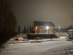 A wooden cabin with a porch and a bench, surrounded by snow and trees.