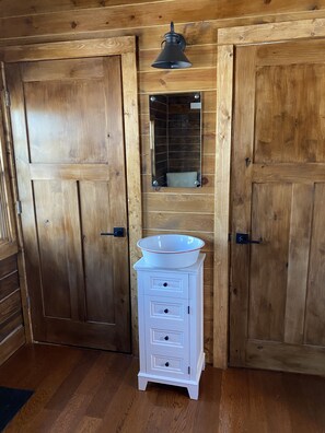 A wooden-paneled room with two large doors, a white cabinet with drawers, and a mirror above a sink.
