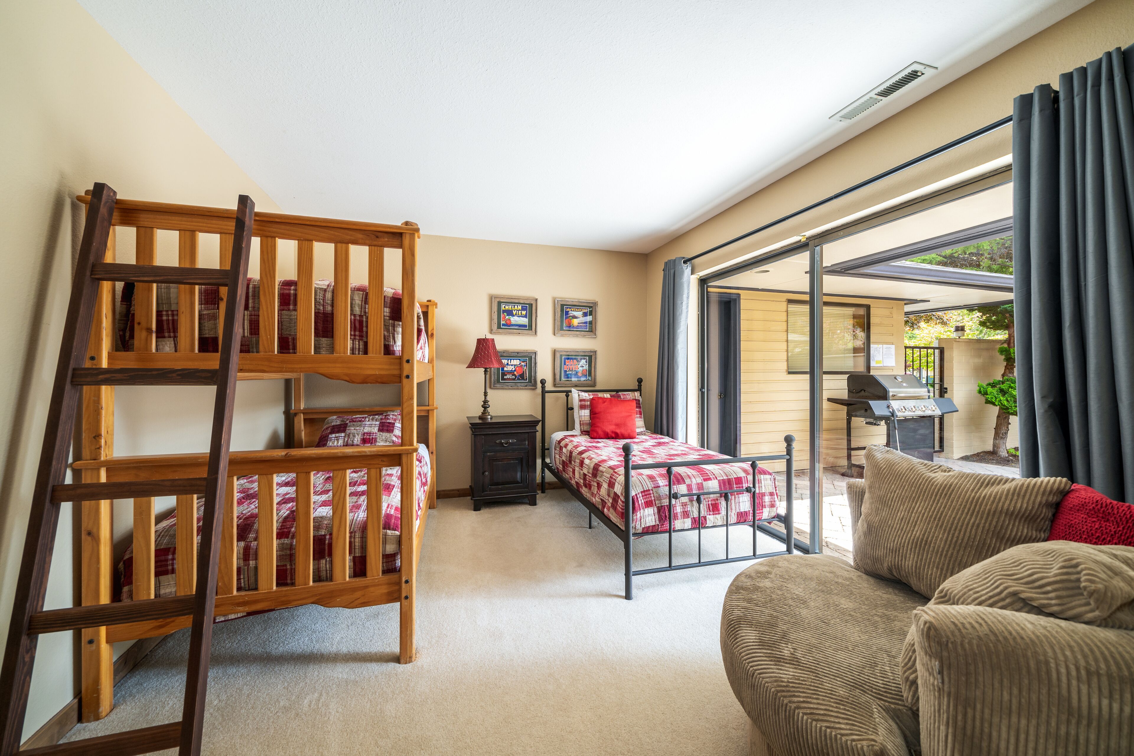 A bedroom with a bunk bed, a single bed, a nightstand, a lamp, and a window with curtains.