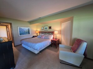 Une chambre d’hôtel avec un lit, des tables de chevet, une chaise, un bureau et un tableau au mur.