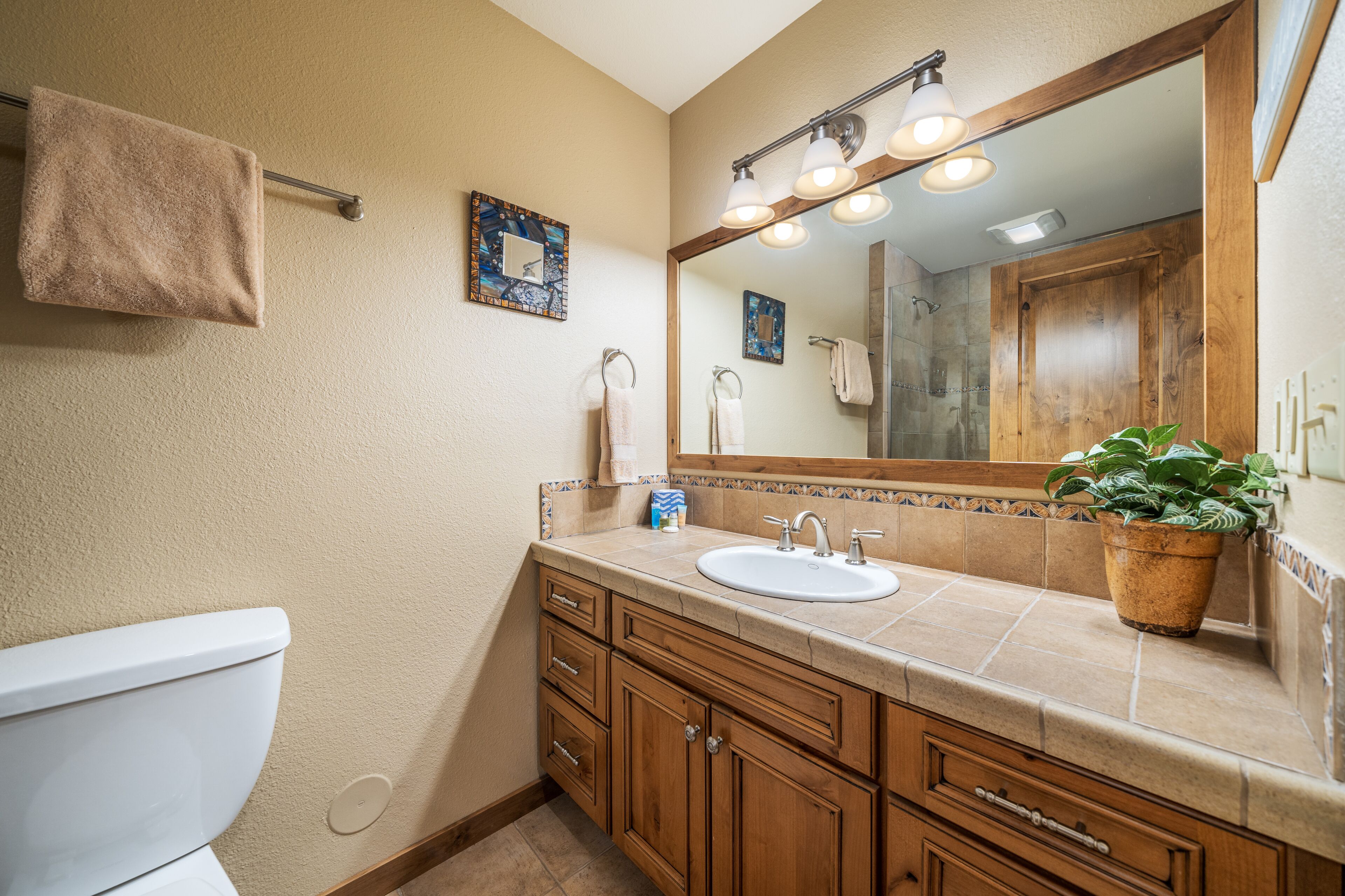 A bathroom with a toilet, sink, vanity, and a large mirror.