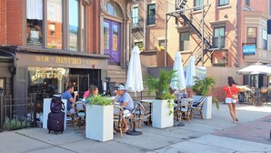 An outdoor cafe with tables and chairs, a sign for a bar and bistro, and a building with a fire escape. - Modern, Smart 1Bed -Private Entry. Boston's Best Location Close to Everything (Boston)