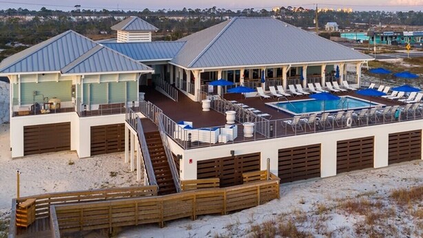 Un resort frente a la playa con piscina, sillas de descanso y terraza cubierta.
