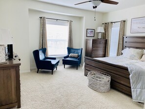 Een slaapkamer met een bed, twee stoelen, een kaptafel, een lamp en een plafondventilator.