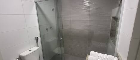 A modern bathroom with a glass-enclosed shower, a toilet, and a granite countertop with a towel.