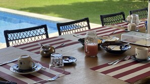 Een ontbijttafel, gedekt met uitzicht op een zwembad en een houten hek op de achtergrond.