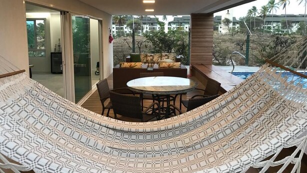 Een hangmat met een geometrisch patroon, een ronde tafel met stoelen en uitzicht op een zwembad en palmbomen.