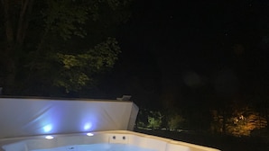 A hot tub with a lid open, surrounded by trees and a dark background. - Hillside Haven Historic Vacation Home in Deersville by Tappan & Clendening Lakes (Deersville)