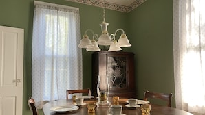 A dining room with a round table set for four, a cabinet with glass doors, and a floral-patterned window with sheer curtains. - Hillside Haven Historic Vacation Home in Deersville by Tappan & Clendening Lakes (Deersville)