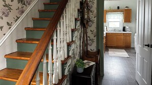 A staircase with wooden steps and white balusters leading to a kitchen area with wooden cabinets and a window. - Hillside Haven Historic Vacation Home in Deersville by Tappan & Clendening Lakes (Deersville)