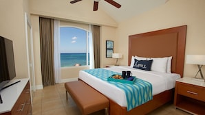 Habitación de hotel con cama, un banco, televisor, escritorio y ventana con vista al océano.