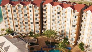 Un hotel con varias torres, una zona de piscina central con palmeras y tumbonas.