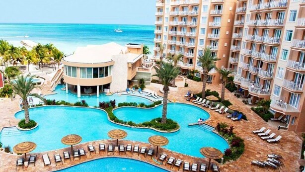 Un resort con una amplia piscina central, varios balcones y vista al océano.