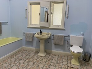 A bathroom with a yellow bathtub, a pedestal sink, a toilet, and a window above the sink. - Abbey Beach Oasis (Abbey)