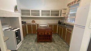 A compact kitchen with a stove, oven, and refrigerator. It features wooden cabinets, a tiled floor, and a central island.