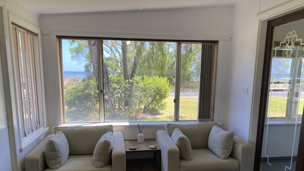 A room with two beige sofas facing a large window with a view of trees and a body of water.