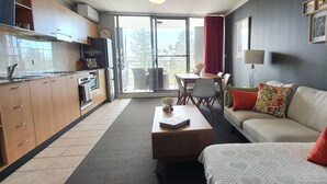 A modern kitchen with a dining area, a sofa with colorful cushions, and a view through a glass door. - Oceanview Escape at The Entrance (The Entrance)