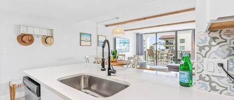 A modern kitchen with a large island, stainless steel sink, and a dining area with a view of the ocean.