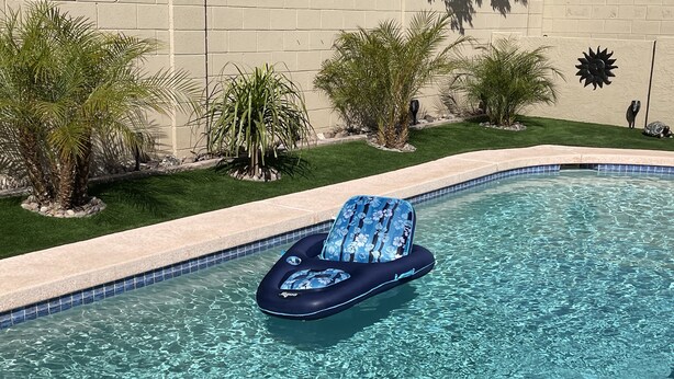 Uma piscina cristalina com uma espreguiçadeira flutuando na água.