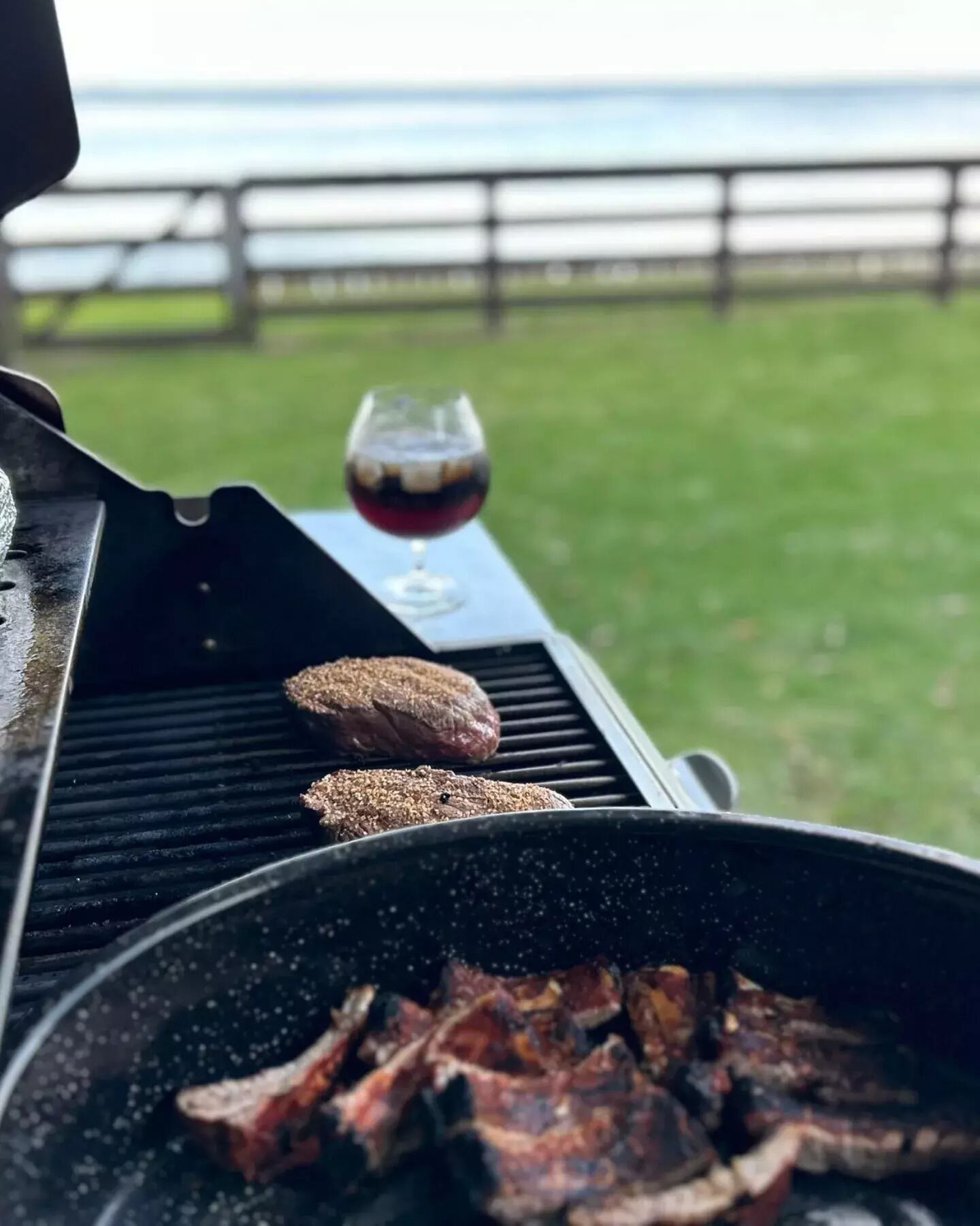Ein Grill mit Hamburgern und einem Glas Rotwein, draußen mit Blick auf den Ozean.