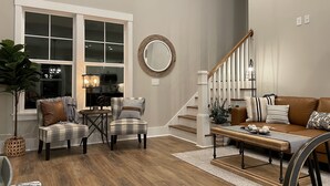 Un salon comprenant un canapé, des fauteuils, une table basse, un escalier et une grande fenêtre.