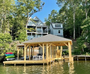 A wooden dock extending into a lake with a covered seating area and kayaks. - 💥Incredible Sunset Views💥New Build💥Large Boathouse!💥Kayaks & More Included!! (Henrico)