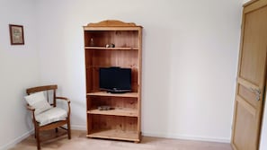 A wooden TV stand with a television, a chair with a cushion, and a door.