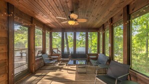 Eine Holzterrasse mit Deckenventilator, großen Fenstern und Sitzgelegenheiten im Freien.