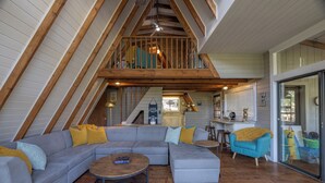 A loft-style living room with a large gray sectional sofa, a round coffee table, and a blue armchair. A wooden staircase leads to an upper level. - Rae of Sunshine by Innsbrook Vacations! (Innsbrook)