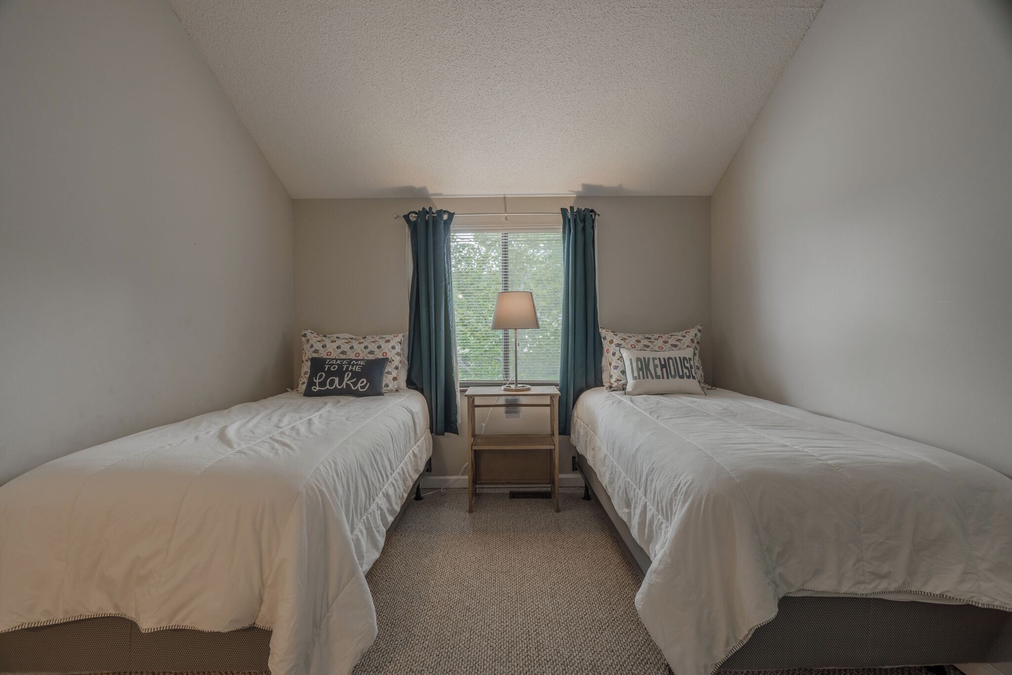 A bedroom with two single beds, a nightstand, a lamp, and a window with curtains.