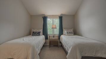A bedroom with two single beds, a nightstand, a lamp, and a window with curtains.