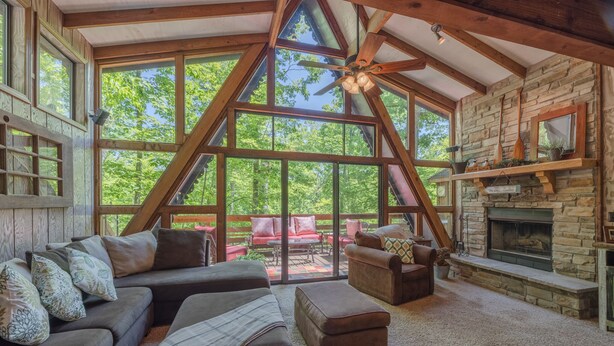 A spacious living room with a stone fireplace, large windows, and a ceiling fan. - Snug Harbor by Innsbrook Vacations! (Innsbrook)
