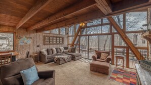 A cozy cabin interior with a wooden ceiling, large windows, a sectional sofa, and a dining area. - Snug Harbor by Innsbrook Vacations! (Innsbrook)