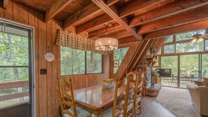 Un comedor de madera con una mesa, sillas, una araña y vistas al exterior.