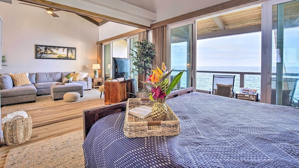 A spacious living area with a large bed, a sofa, and a television. There is a view of the ocean through large windows. - Airy Oceanfront Kailua-Kona Gem w/ Community Pool (Kailua-Kona)