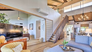 A spacious living area with a large flat-screen TV, comfortable seating, a wooden staircase, and a kitchen in the background. - Airy Oceanfront Kailua-Kona Gem w/ Community Pool (Kailua-Kona)