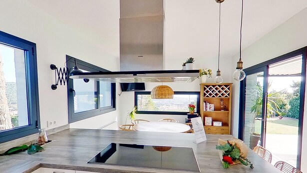 A modern kitchen with a central island, a dining area with wicker chairs, and a view of the outdoors.
