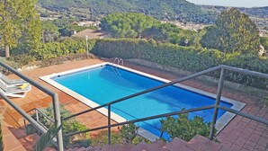 A rectangular swimming pool with a metal safety railing, surrounded by a brick deck and lush greenery.