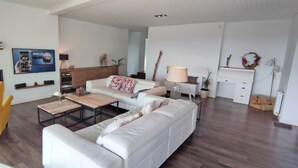 A modern living room with a sofa, coffee table, and a yellow armchair. There is a fireplace, a TV, and a wall-mounted shelf with decorative items.