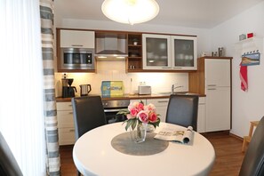 A compact kitchen with modern appliances, a dining table with chairs, and a small refrigerator. - Haffblick Whg. Ha18, Deutschland (Ostseebad Boltenhagen)