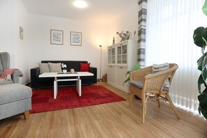 A living room with a sofa, a coffee table, a wicker chair, a cabinet, and a red rug. - Haffblick Whg. Ha18, Deutschland (Ostseebad Boltenhagen)
