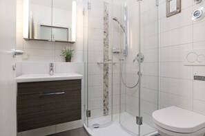Ein modernes Badezimmer mit einer gläsernen Duschkabine, einem weißen Waschbecken und einem dunklen Holz-Badmöbel.